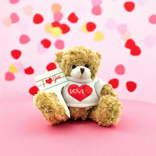 Teddy bear with 'I Love You' sign and heart on pink background