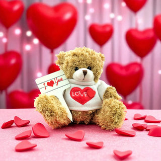 Teddy bear holding a 'I Love You' card with red heart decorations on a pink background