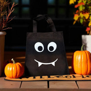 Black tote bag with a smiley face design on a doormat with pumpkins and autumn decorations.