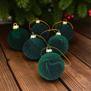 Green velvet Christmas ornaments on a wooden surface with a blurred Christmas tree in the background.