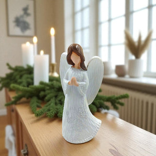 White angel figurine on a wooden surface with candles and greenery in the background