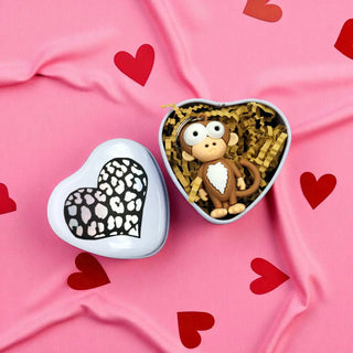 Heart-shaped box with a monkey figurine on a pink fabric background with red hearts.