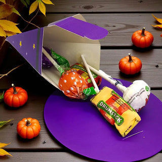 Halloween-themed lollipops on a purple stand with pumpkins and leaves on a wooden surface.