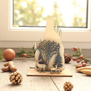 Wooden decorative piece with deer and trees on a wooden surface with festive decorations. Woodlands, Nordic Aesthetic