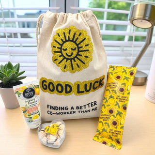 Good luck gift bag with sun design, hand cream, and sunflower-themed items on a desk.