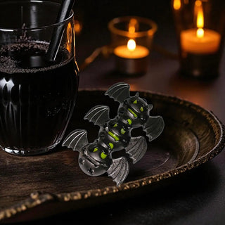 Black bat-shaped cookie cutter on a wooden board with a glass of dark liquid and candles in the background.