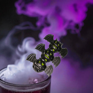 Bat-shaped drink stirrer with glowing eyes in a glass of red liquid with smoke on a dark background