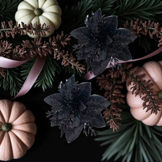 Decorative arrangement with black flowers, pumpkins, and greenery on a dark background