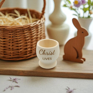 Decorative egg cup text on a wooden surface with a wicker basket and wooden rabbit in the background.