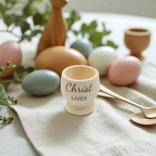 Egg cup with  text on a table with pastel Easter eggs and greenery.