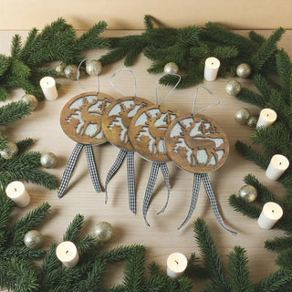 Wooden reindeer ornaments with checkered ribbons on a wooden surface surrounded by greenery and candles.