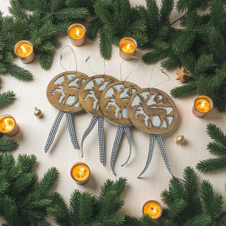 Wooden reindeer ornaments with checkered ribbons surrounded by candles and pine branches on a light background