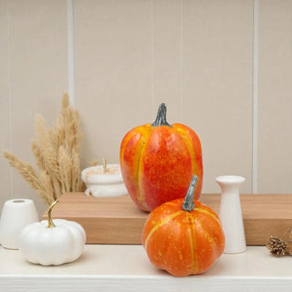 Two decorative pumpkins on a shelf with white vases and a wooden board in the background.