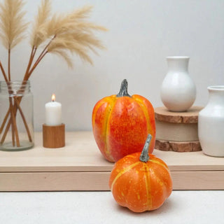 Two small pumpkins on a surface with decorative items in the background.