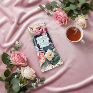 Floral-themed product packaging on a pink surface with tea and flowers