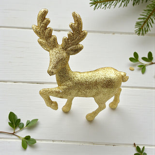 Gold deer ornament on a white wooden surface with green leaves. Nordic Aesthetic