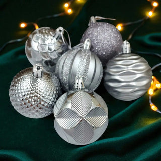 Silver Christmas ornaments with textured patterns on a dark green fabric background with string lights.
