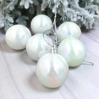 Set of pearl-like Christmas ornaments on a white surface with a blurred green leafy background