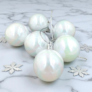 Set of pearl-like Christmas ornaments on a marble surface with decorative snowflakes.