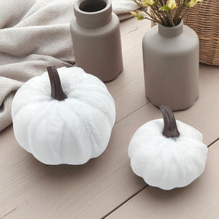 Two white pumpkins on a wooden surface with two gray vases and a basket in the background.
