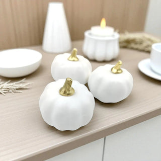 Three white pumpkins with gold stems on a wooden surface.