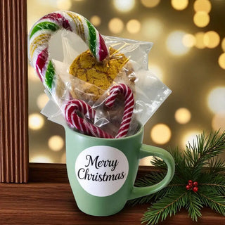 Green mug with 'Merry Christmas' label filled with cookies and candy canes, against a blurred festive background.