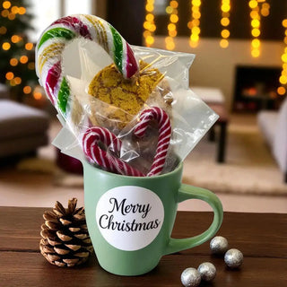 Green mug with 'Merry Christmas' label, candy canes, cookies, and pine cone on a festive background.