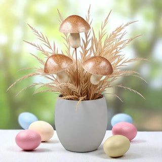 Decorative arrangement with mushrooms and grass in a pot, surrounded by pastel-colored eggs on a blurred natural background.