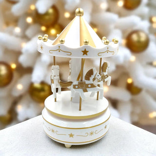 Decorative carousel toy with gold accents on a white surface, blurred Christmas tree in the background.
