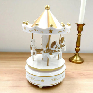 White and gold carousel toy on a wooden surface with a candle in the background