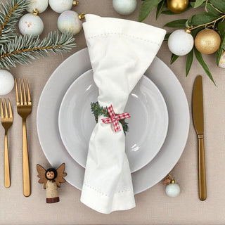 Christmas table setting with white napkin, gold cutlery, and festive decorations.
