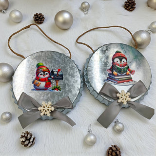 Two Christmas-themed decorations with penguins and snowflakes on a white surface with ornaments.