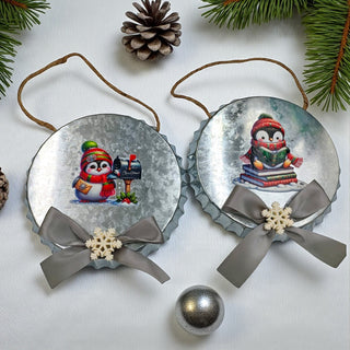 Two Christmas-themed penguin ornaments with ribbons on a white background with pine branches.