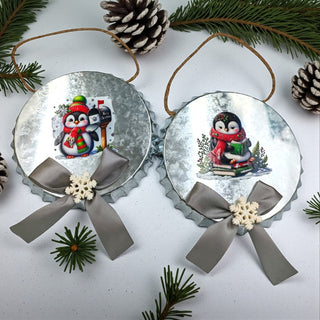 Two Christmas ornaments with penguin designs on a white background with pine branches and pinecones.