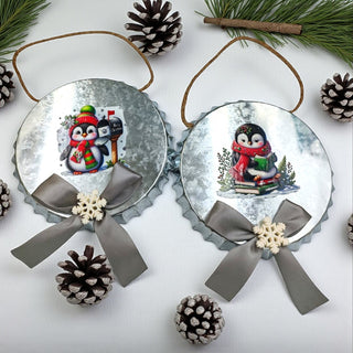 Two Christmas ornaments with penguin designs on a white background with pine branches and pinecones.