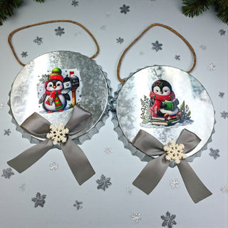 Two Christmas ornaments with penguin designs on a white background with pine branches and pinecones.