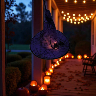Hanging black spider web decoration on a porch with Halloween lights and pumpkins.