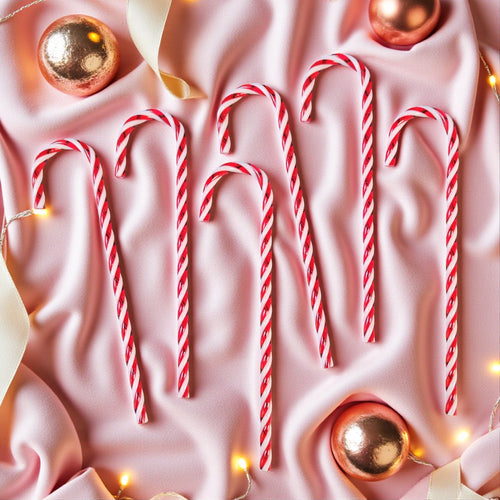 Red and white candy canes on a pink fabric background with gold ornaments and lights.