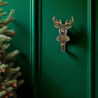 Decorative deer head knocker on a green door with a Christmas tree to the left.