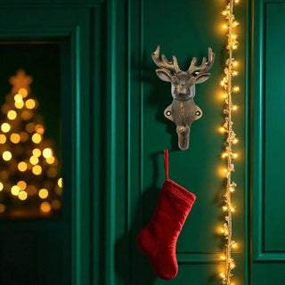 Decorative deer head hook with a red stocking on a green door with Christmas lights and tree in the background.