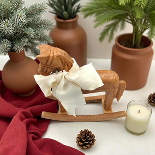 Wooden reindeer figure with a bow, surrounded by potted plants and a candle on a white surface.