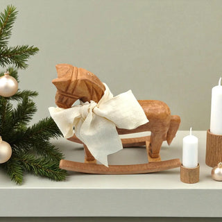 Wooden rocking horse with a bow, Christmas tree, and candles on a shelf.