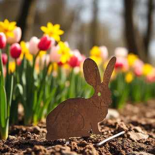 Metal rabbit ornament on soil with colorful tulips in the background
