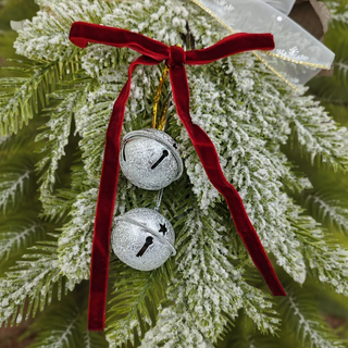 Decorative silver jingle bells with a red ribbon on a frosted green branch.