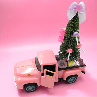 Pink toy truck with a Christmas tree and candy on a pink background