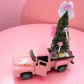 Pink toy truck carrying a small Christmas tree with candy decorations on a pink background