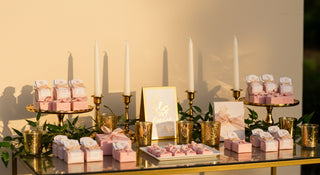 Table setting with pink boxes, candles, and a card on a neutral background