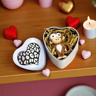 Heart-shaped box with a monkey figurine and leopard print heart on a wooden surface with decorative hearts and a candle.